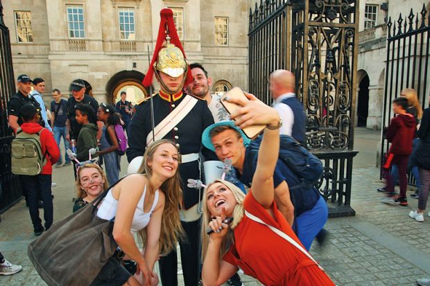 King's guard stands to attention guarding the entrance to the Horse Parade while tourists take a selfie to illustrate Age of the influencer?